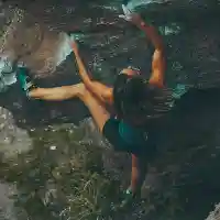 A young, fit woman free climbing up a rocky mountain face