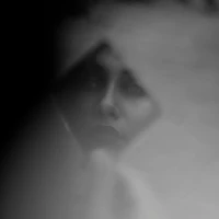 Man's hand holding a diamond shaped mirror with the face of a woman in it